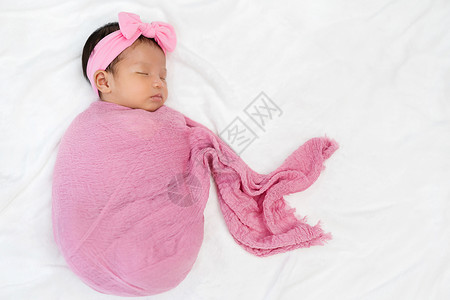 新生婴儿睡在床上的粉色布织毯子中高清图片