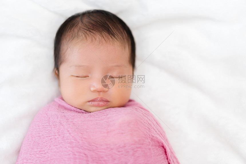 新生婴儿睡在床上的粉色布织毯子中图片