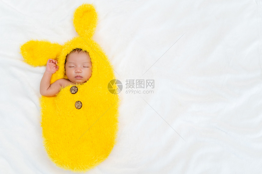 穿着兔子皮西装的新生儿婴睡在床上图片