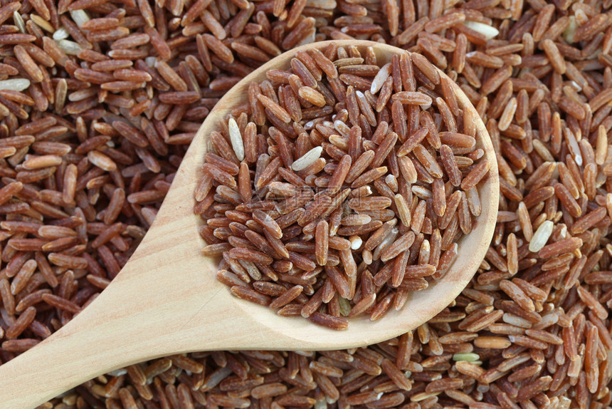 木勺中的有机棕色大米放在草粒谷物大米上自然食物背景图片