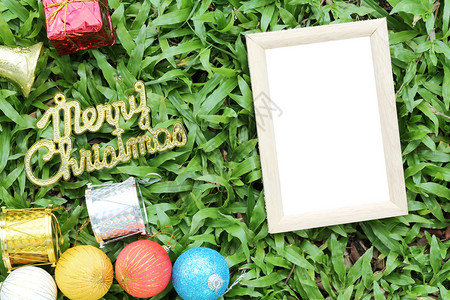 在绿草坪上的圣诞装饰品上面有圣诞快乐的金条地板上有空木框图片