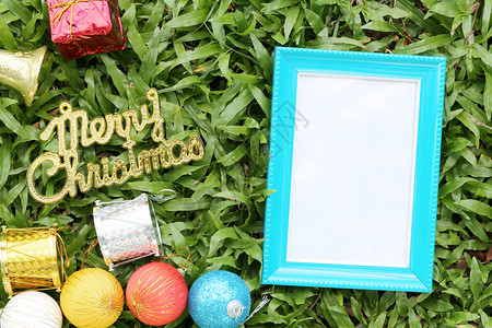 在绿草坪上的圣诞装饰品上面有圣诞快乐的金色文字地板上有蓝色的空木框图片