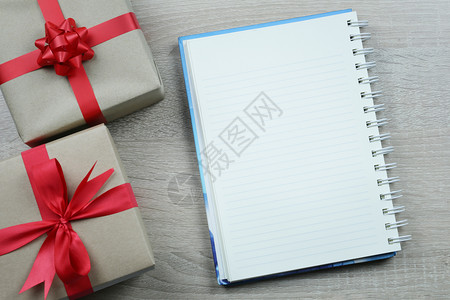 棕色礼品盒和用于圣诞装饰的空笔记本纸放在木制地板背景上有复制空间图片