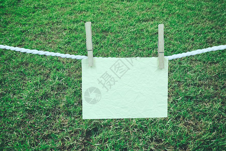 空白纸挂在绳子和绿草坪背景上图片