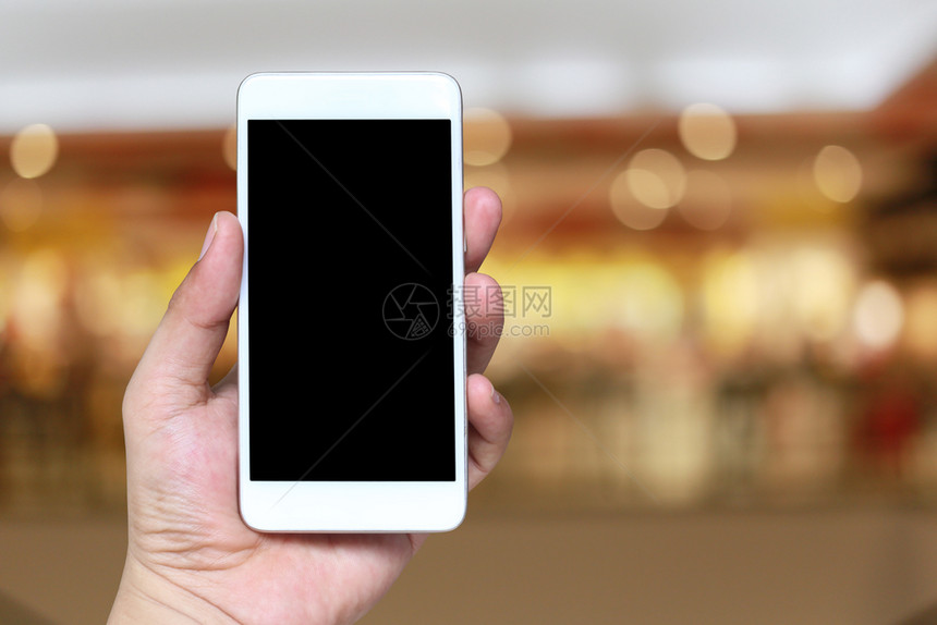 手持智能机设备的人在模糊购物商场背景并在屏幕上有白色的复制空间图片