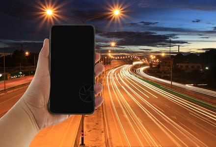 一个人的手有空屏幕智能手机和夜晚高速公路的背景图片