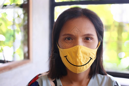 亚裔妇女带着微笑的面具保护她们不受新冠或新冠健康护理概念的影响图片