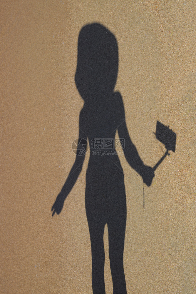 沙滩上一个拿着自拍棒的女孩的影子在沙滩上自拍沙滩上一个拿着自拍棒的女孩的影子海滩上的自拍图片