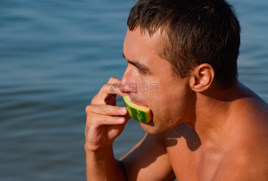 一个人正在吃坐海滩上的西瓜一个成熟的西瓜在一个人的手中正在吃坐海滩上的西瓜一个成熟的西瓜在一个人的手中图片