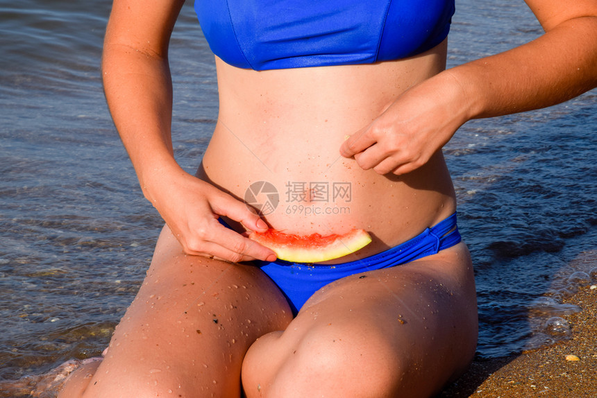 一个女人拿着块西瓜坐在沙滩上一只成熟的西瓜在金发女郎手里图片