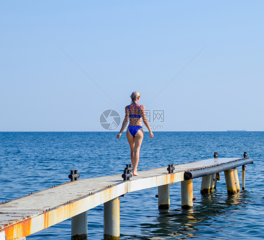 一个穿着蓝色比基尼的漂亮女孩走过码头走向大海海工混凝土桥墩从码头跳入水中漂亮的战利品女孩一个穿着蓝色比基尼的漂亮女孩走过码头走向图片