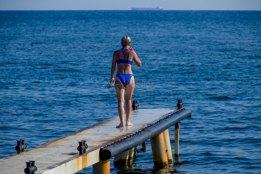 一个穿着蓝色比基尼的漂亮女孩走过码头走向大海海工混凝土桥墩从码头跳入水中漂亮的战利品女孩一个穿着蓝色比基尼的漂亮女孩走过码头走向图片