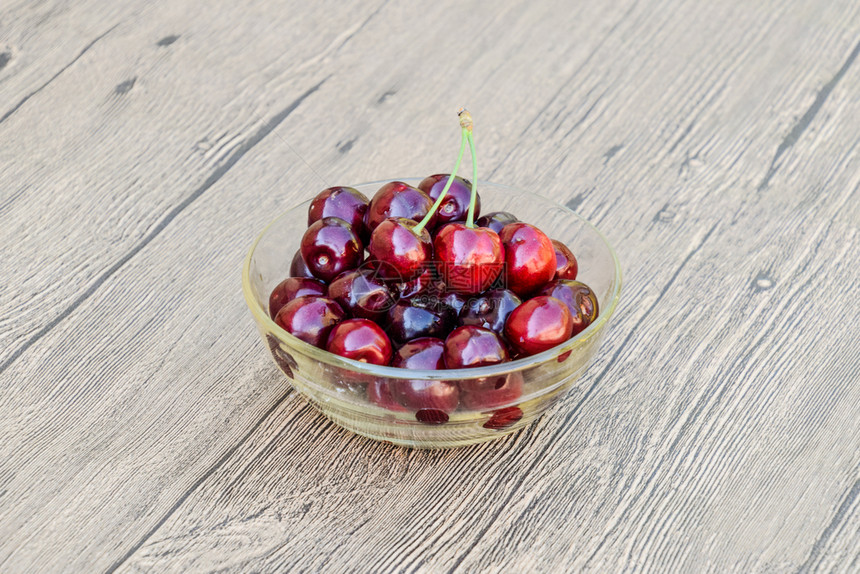 一种甜樱桃的浆果放在木制背景上的玻璃碗里成熟的红甜樱桃一种甜樱桃的浆果放在木制背景上的玻璃碗里成熟的红甜樱桃图片