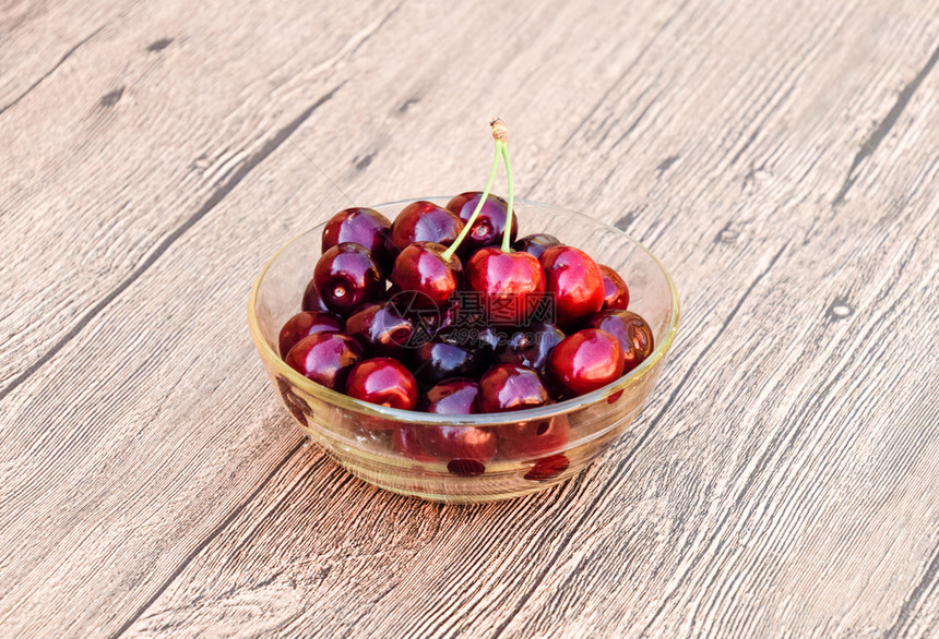 一种甜樱桃的浆果放在木制背景上的玻璃碗里成熟的红甜樱桃一种甜樱桃的浆果放在木制背景上的玻璃碗里成熟的红甜樱桃图片