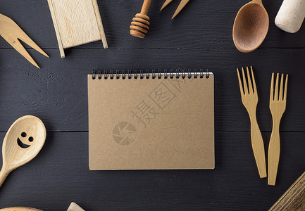 黑桌上木制厨房物品中间空白页的开放笔记本图片