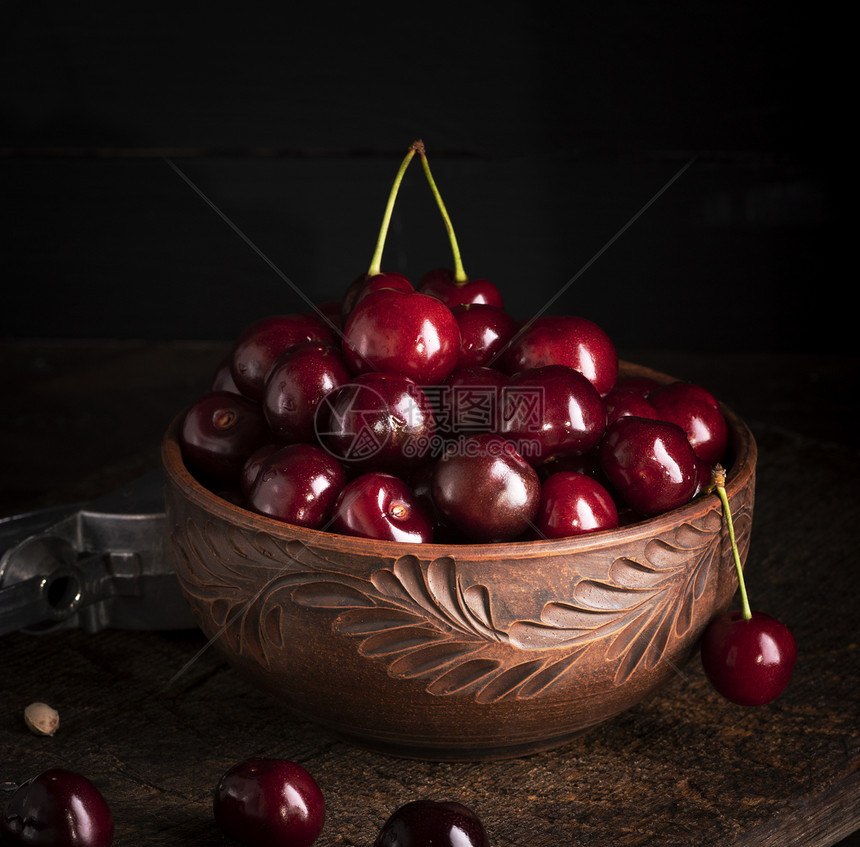 成熟的红多汁甜樱桃在木制桌子上的棕土碗里图片