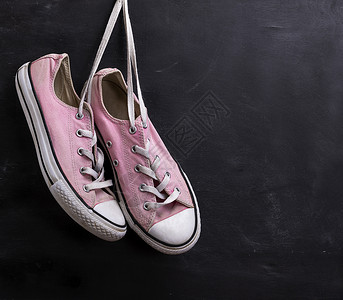 一对粉红色的纺织运动鞋挂在黑色背景的带子上复制空间图片