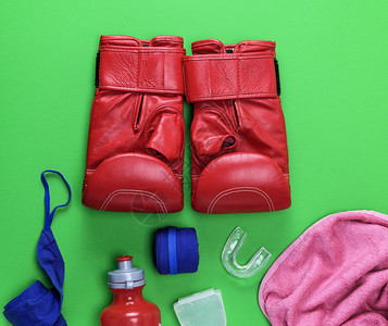 红色皮拳击手套塑料水瓶粉红色毛巾和绿背景的蓝纺织品绷带图片