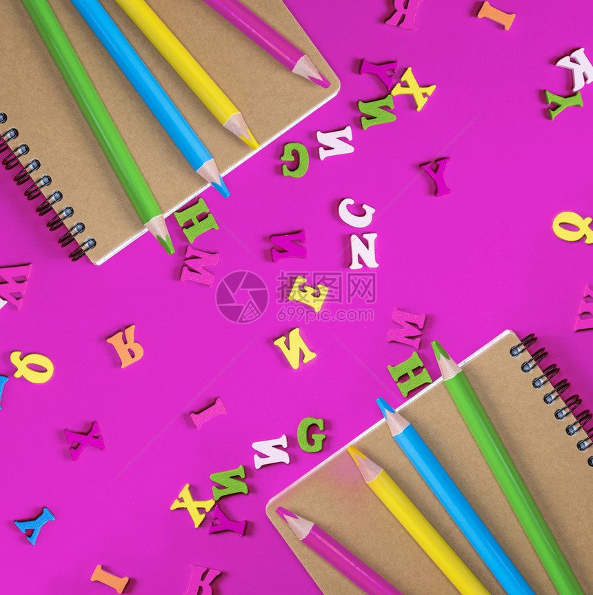 两本笔记和多色木铅笔放在粉红色背景上英文字母散图片