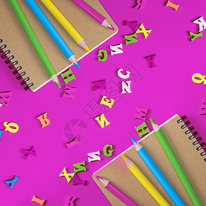 两本笔记和多色木铅笔放在粉红色背景上英文字母散图片