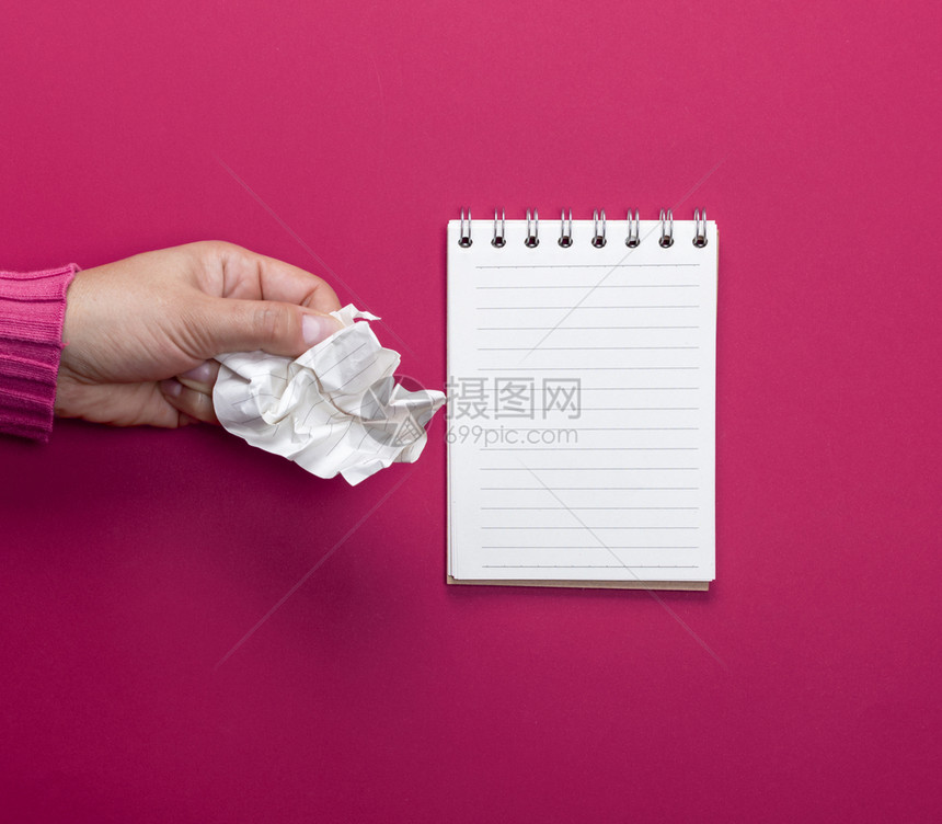 女手拿着一张白色折叠纸和一张粉红色背景的开放笔记本图片