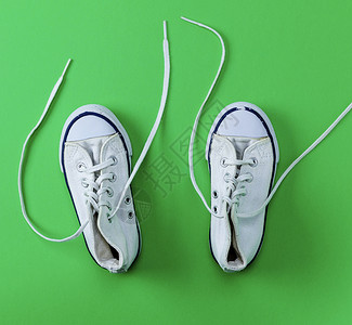 二对白色的旧式纺织运动鞋上面有绿色背景的不松丝带最上视图图片
