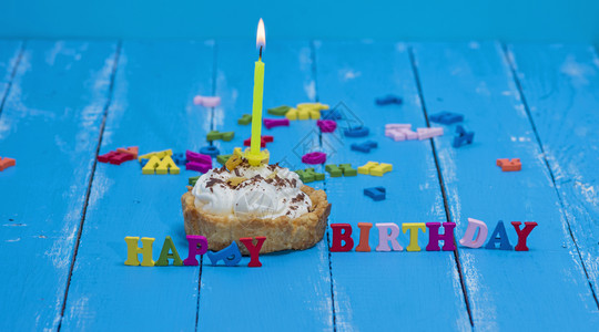 含白奶油的甜蛋糕和蓝木背景的黄蜡烛生日快乐图片