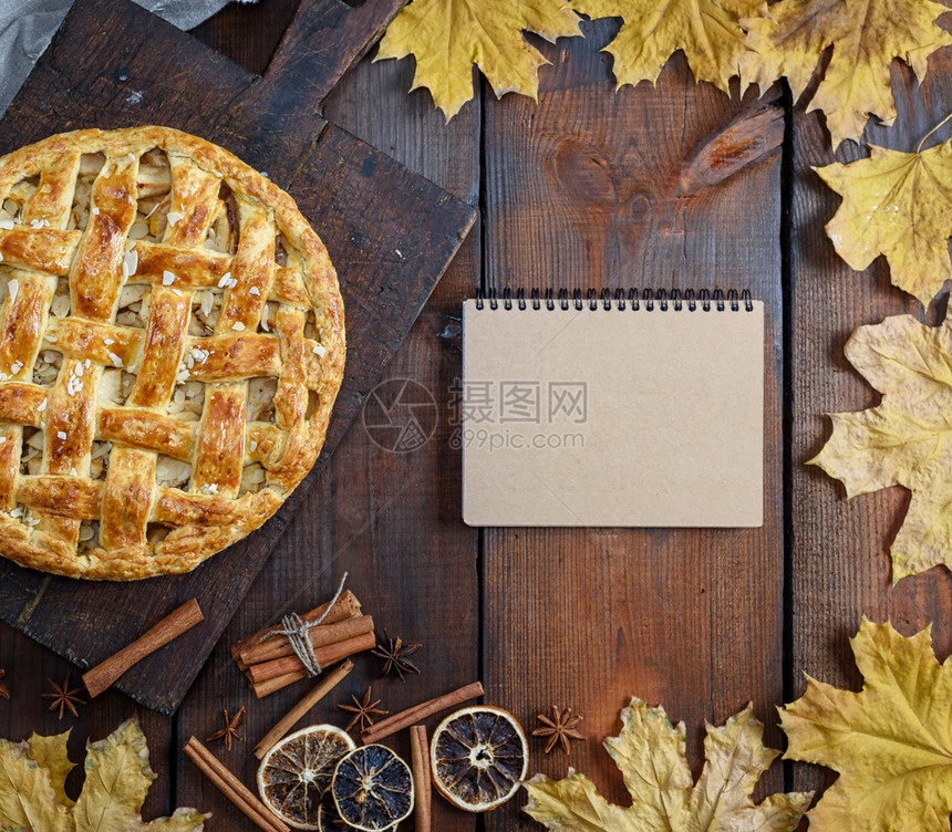 在棕色木板上烤整个圆苹果派泡面糕饼和一张空的纸条上面有食谱的棕色页面图片