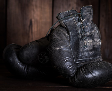 一对非常老旧的黑色皮革拳击手套在棕色木制背景上图片