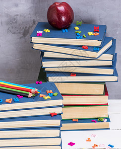 蓝色封面的一堆书多彩木铅笔和红苹果图片