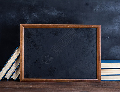 书画框棕色木制桌上的空黑色粉笔画框和堆叠的书背景