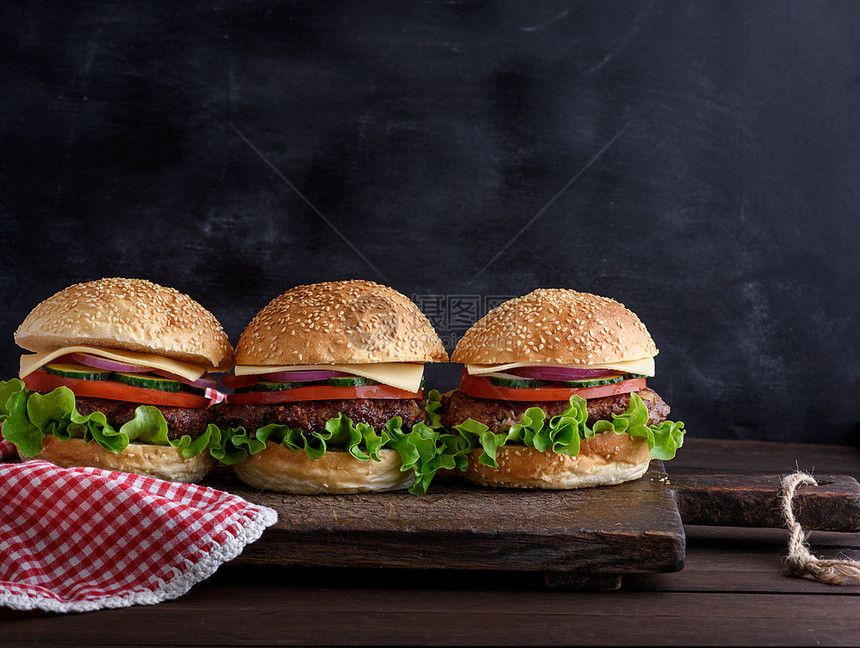 三个汉堡包在棕色木板上加蔬菜黑色背景空间图片