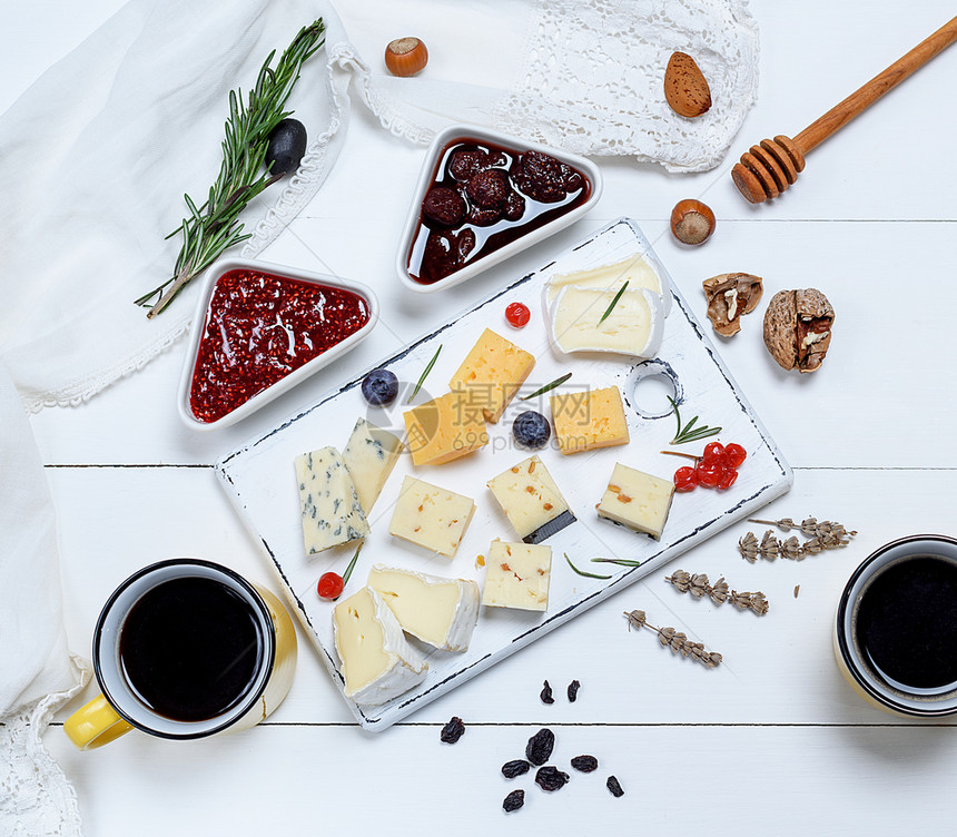 白木板上有小片芝士罗克福特坎伯切达和配有胡桃的奶酪紧靠两个含黑咖啡的黄陶瓷杯子顶层风景图片