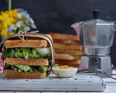 法式吐司三明治和生菜叶子煮鸡蛋一份用纸包在白木板上的素食物图片