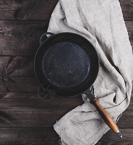 黑色圆煎锅用木柄和灰色的餐巾纸在棕木制桌子上顶视图旧式图片