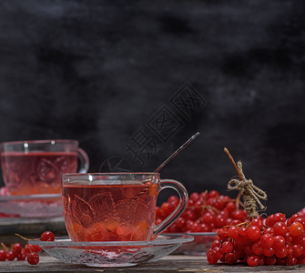 一个透明的杯子里热生茶手柄和碟子在灰色木制桌边新鲜浆果旁图片
