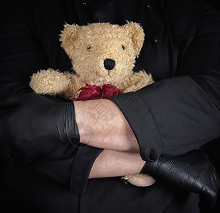 黑衣男子手里拿着棕色泰迪熊黑背景图片