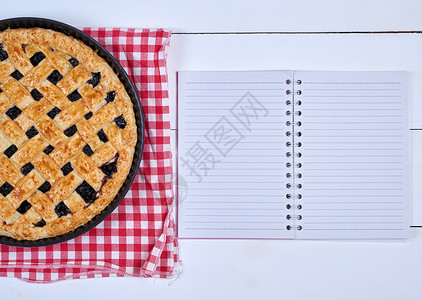 黑色圆卷曲饼和一张开放的笔记本在木形背景顶视图的线条上用空白布排成线图片