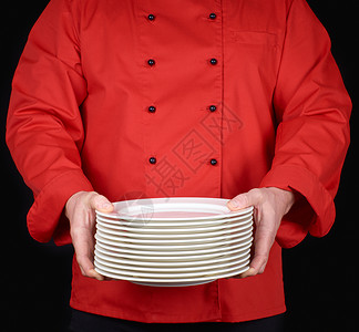 身穿红衣厨服的师手里握着一堆圆白空盘子黑底图片