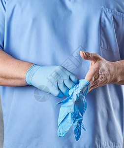 穿蓝制服的医生戴上无菌乳胶手套关上图片