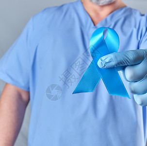 身穿制服和乳胶手套的医生上握着蓝丝带是前列腺癌抗治的象征图片