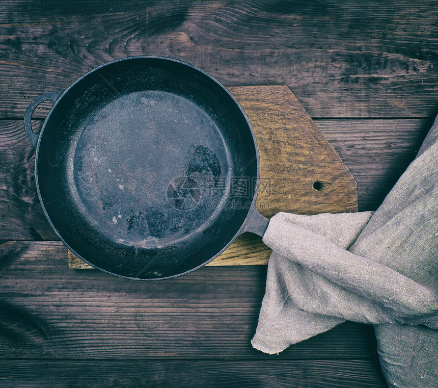 黑色圆煎锅有木制把手和灰色的餐巾纸在棕色木制桌子上顶视图旧式图片