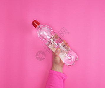 透明塑料瓶在粉红色背景复制空间上用女手的清水装在女手中的塑料瓶图片