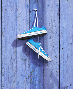 一对蓝色的纺织运动鞋挂在一钉子上墙旧的破碎木板图片