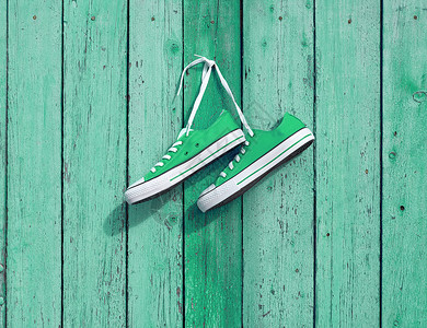 一对绿色的纺织运动鞋挂在墙上的钉子旧破碎木板复制空间图片