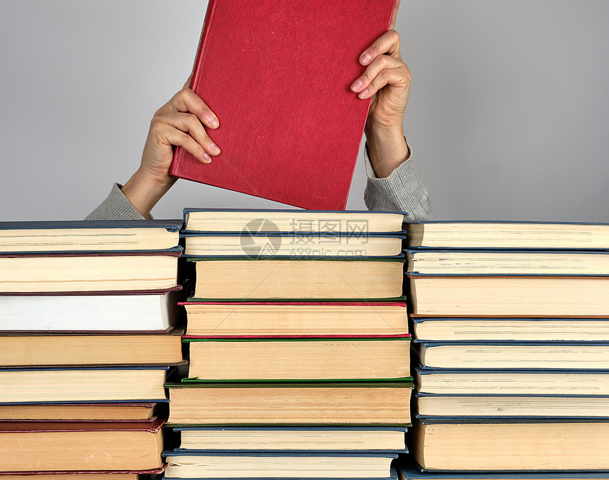 灰色背景的不同书堆手握红色硬封面的书图片
