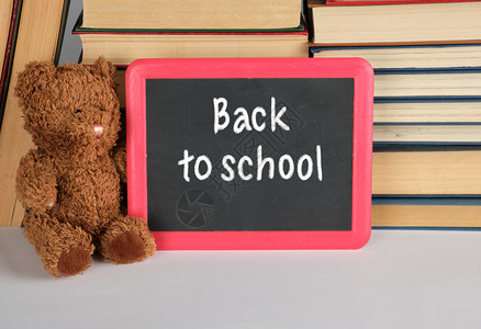 棕褐色泰迪熊和红框的空黑板在一堆书的背景上概念回到学校图片
