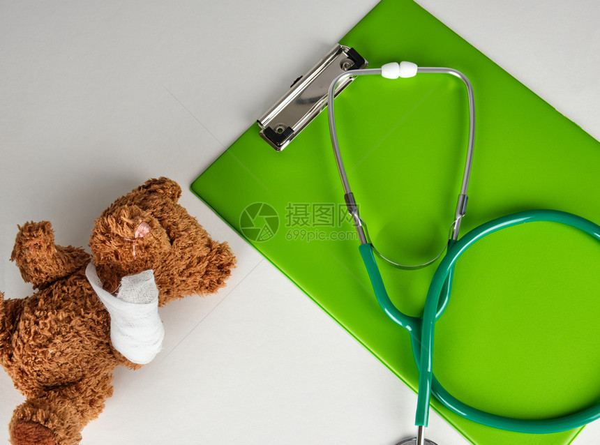 在白色背景泰迪熊旁边的医学听诊镜和绿纸持有者小儿科概念图片