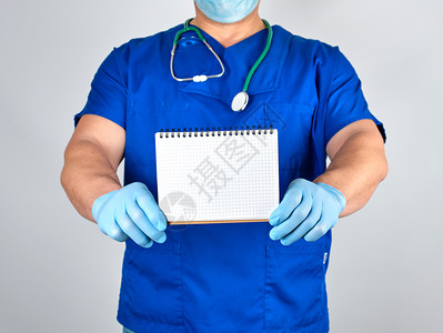 蓝制服医生和无菌乳胶手套持空白笔记本灰色背景图片