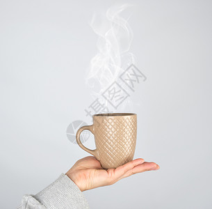 女手握着棕色陶瓷杯子喝着酒灰色的杯子冒出浓蒸汽图片